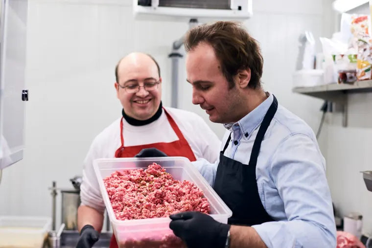 Zwei Mitarbeiter mit frisch gewolftem Fleisch in der Manufaktur
